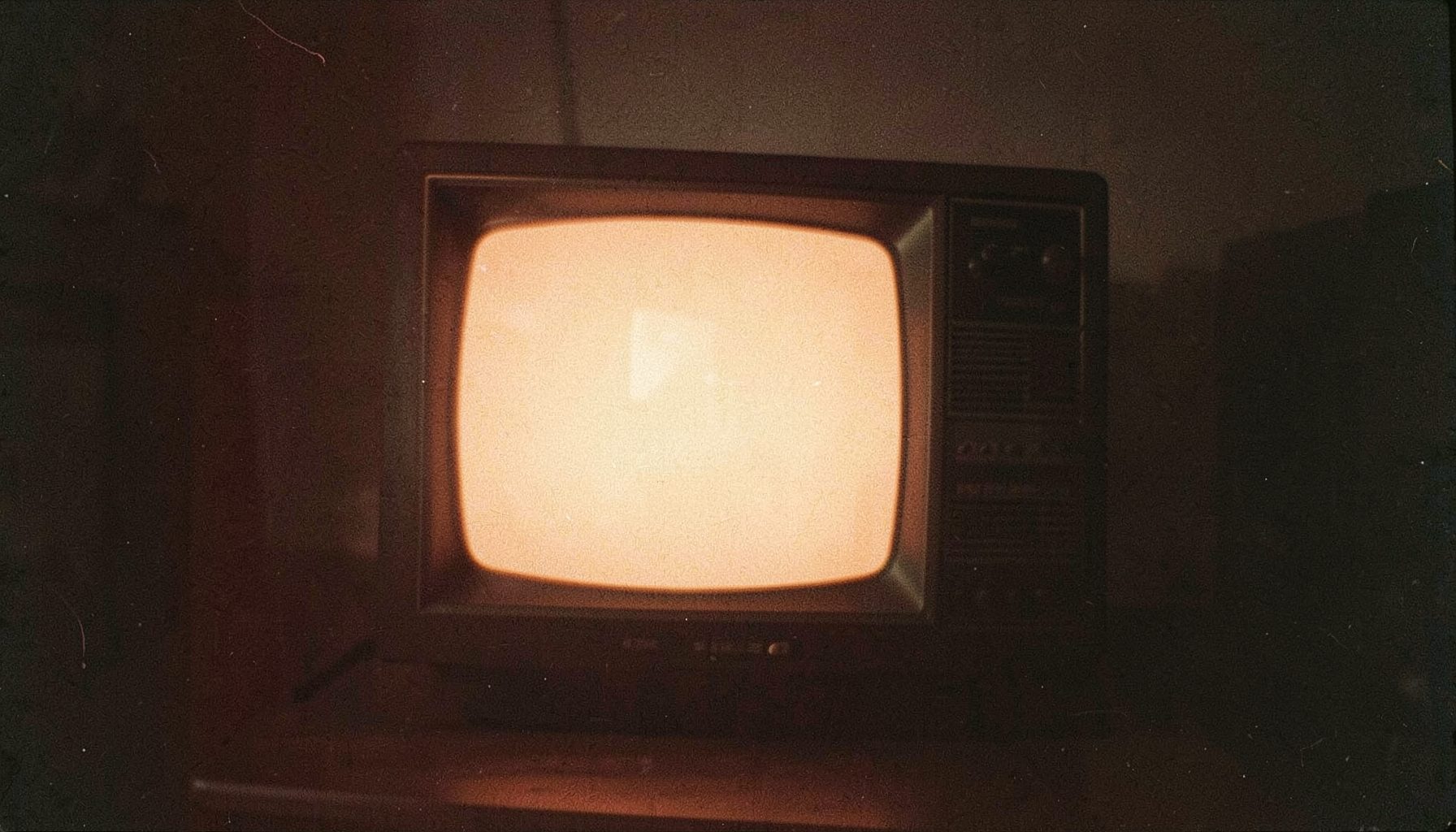 A vintage television set with a warm glowing screen in a dim room, analog film grain, amber and brown tones.