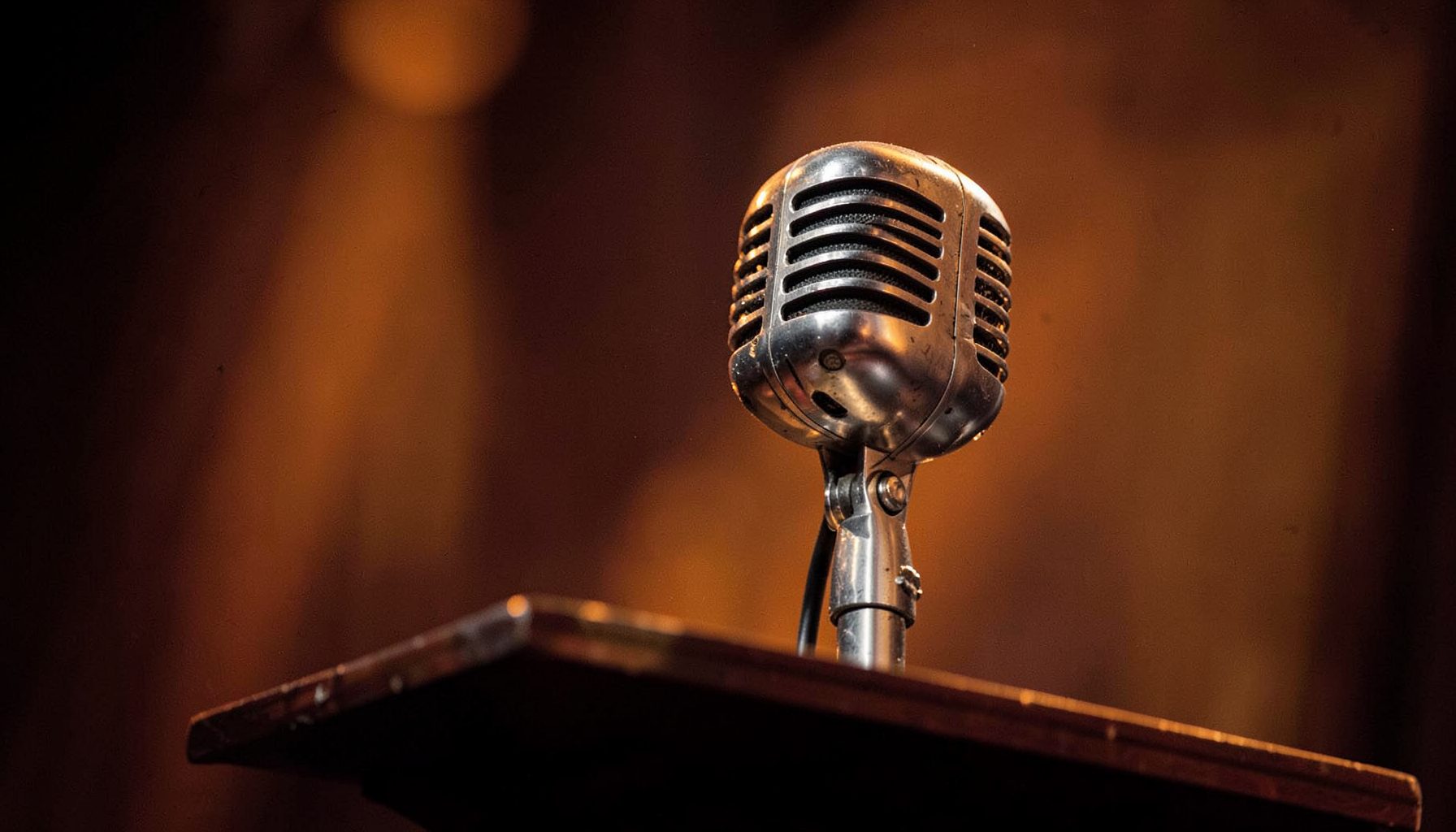 Vintage metallic microphone on a wooden podium, warm brown and orange tones, blurred background
