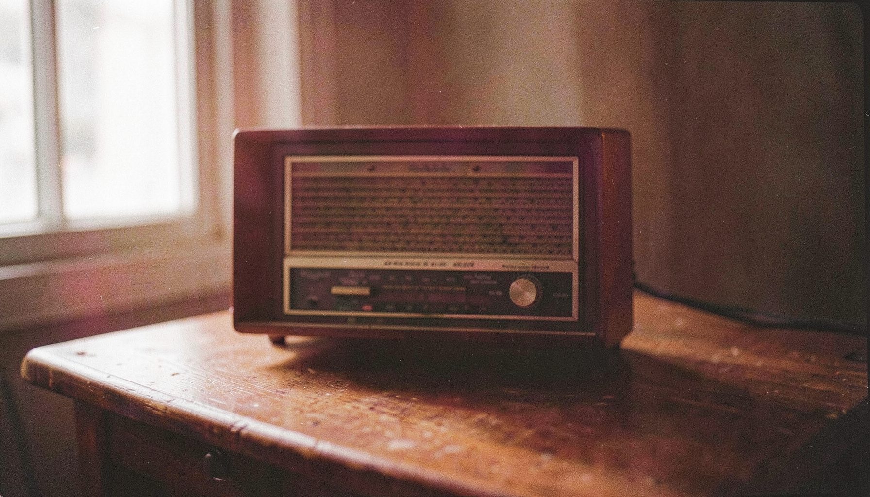 A warm-toned film photograph of a vintage radio on a wooden table, with soft window light and visible grain.