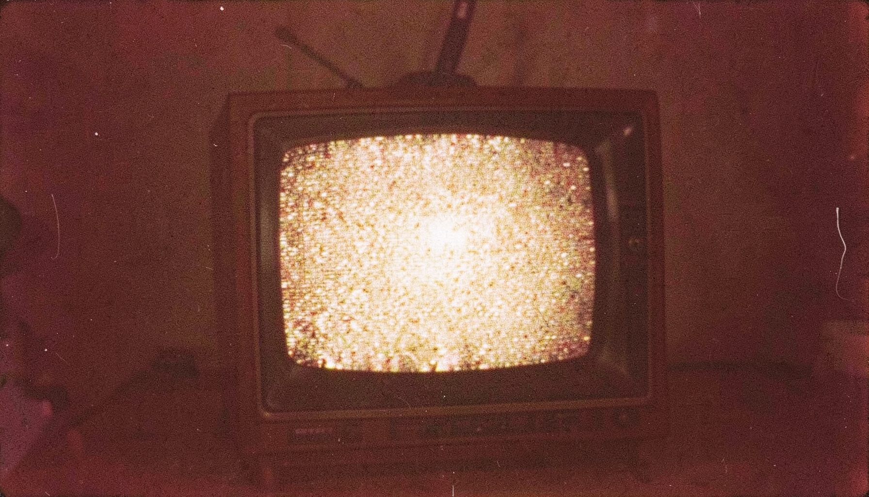 A grainy film photograph of a vintage television set displaying static, warm amber and brown tones, nostalgic mood.